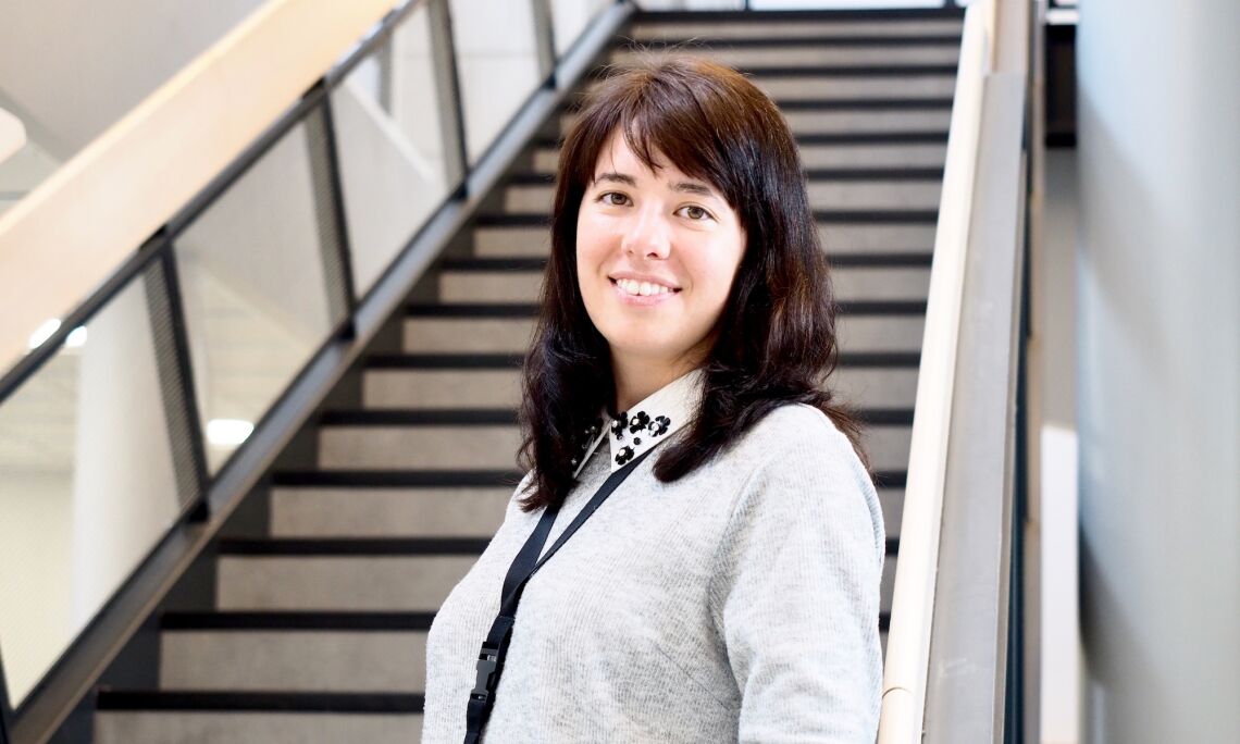 Palveluesimies Tatiana Koshcheeva hymyilee aulatilassa aurinkoisesti, taustalla korkeat portaat.